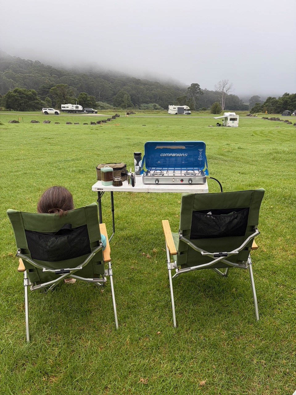 Two camp chairs and a stove facing fog over the grass at Bendeela campground.