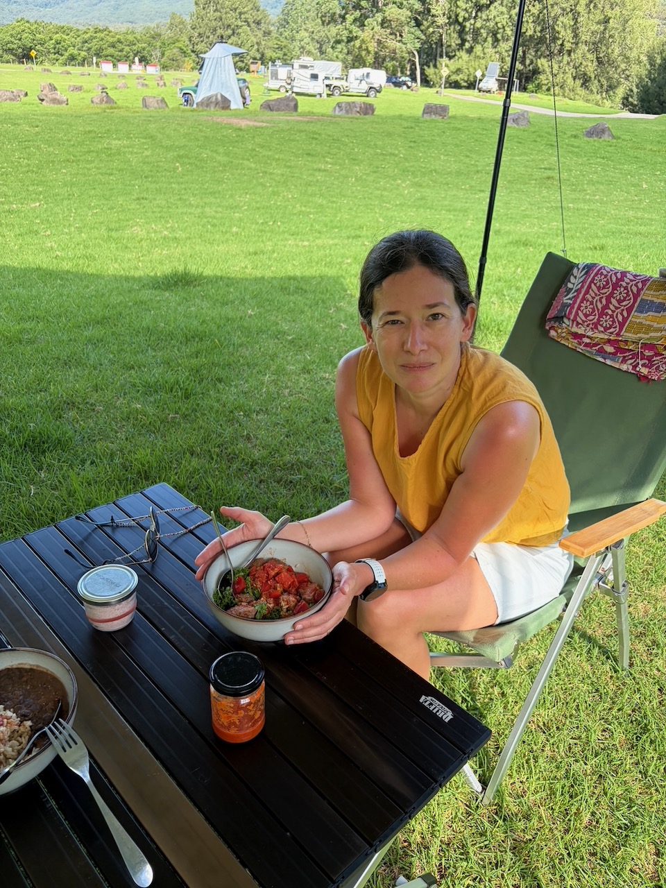 Steph sitting at the camp table holding a bowl of fish curry at Bendeela.