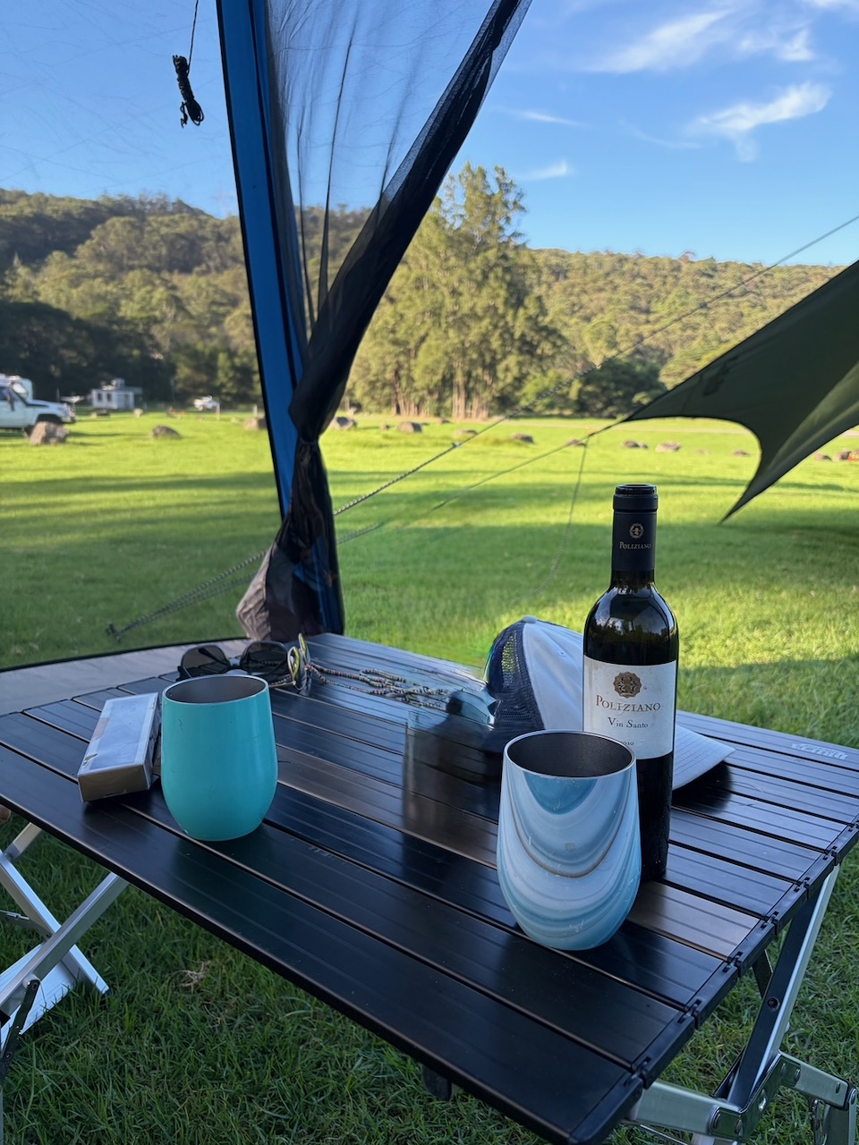 A bottle of dessert wine and two cups on a camp table at Bendeela.