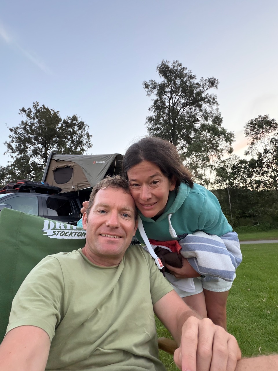 Matt and Steph sitting together at camp with Roger the Ranger and the rooftop tent visible behind them.