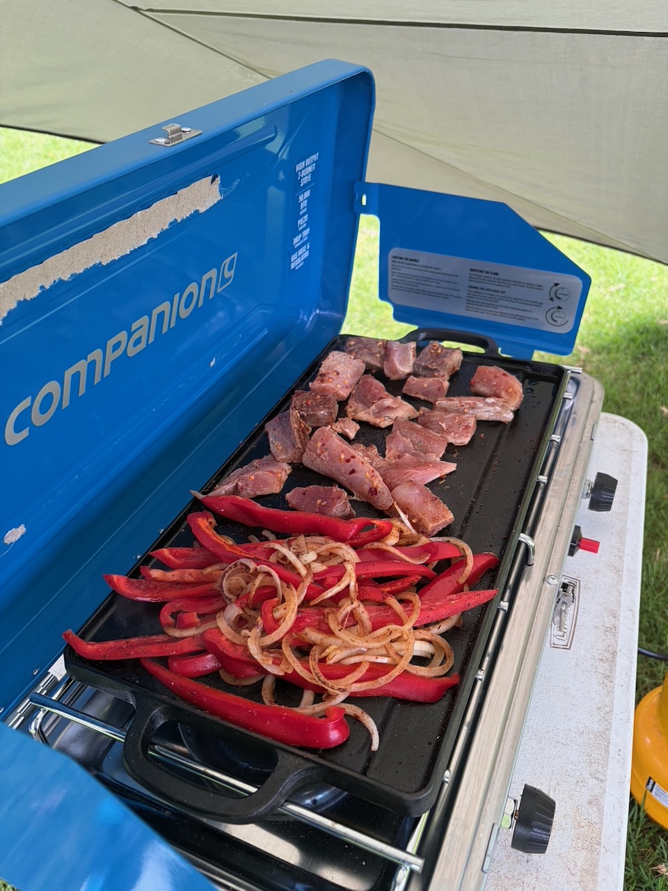 Meat, onions and capsicum cooking on a camp stove hotplate.