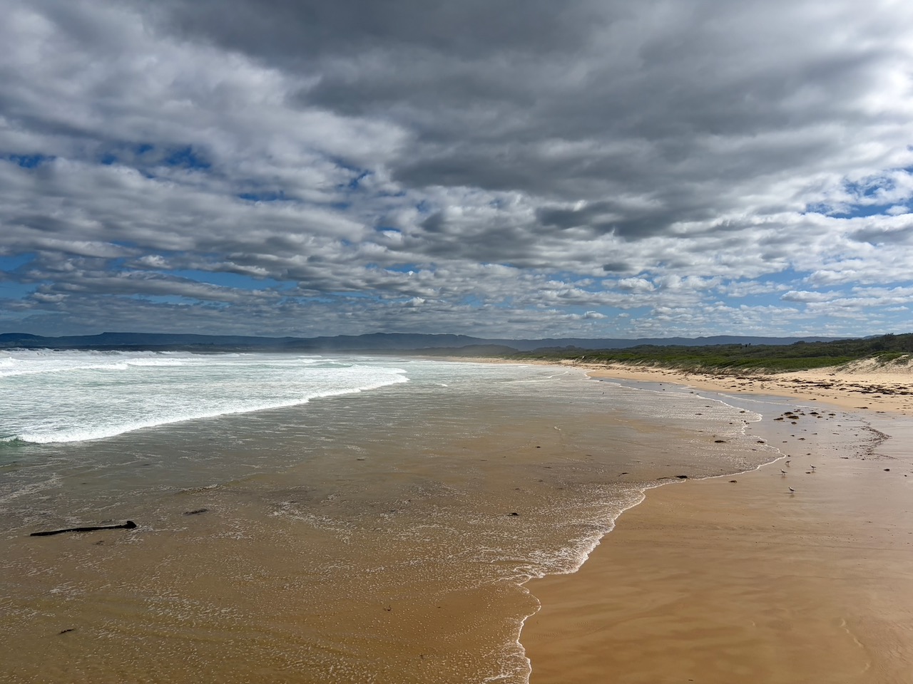A wide empty beach with dramatic clouds and rough surf near Killalea.