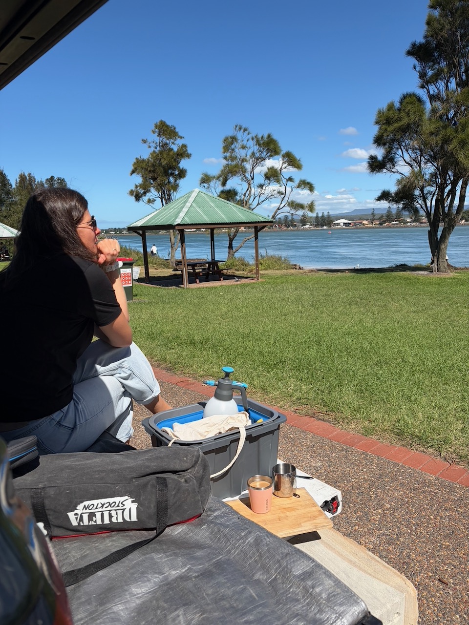 Steph sitting on a low wall with coffee, looking out at the water in Wollongong.