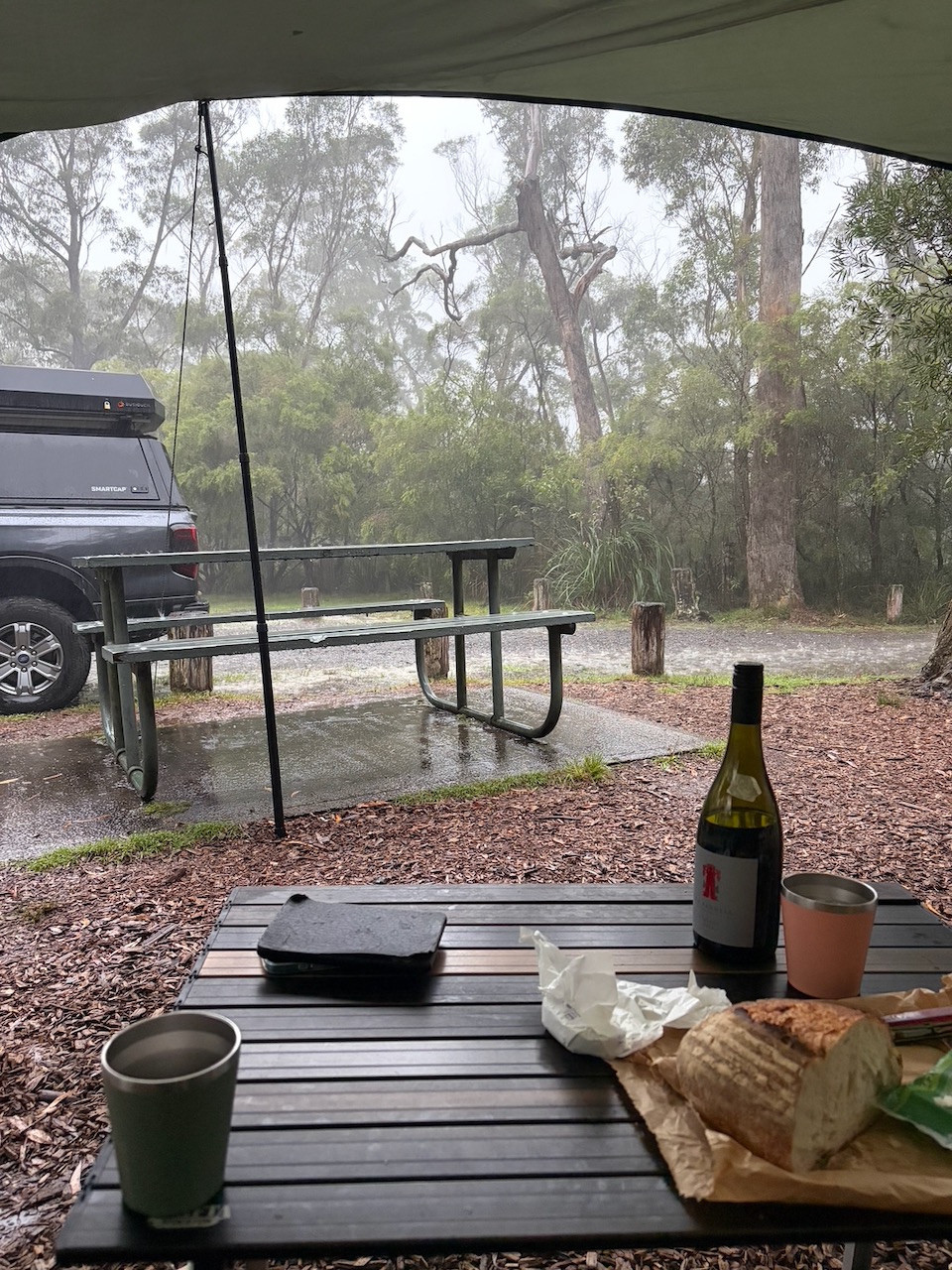 View from under the tarp at Carrington Falls watching torrential rain, with wine and bread on the table.