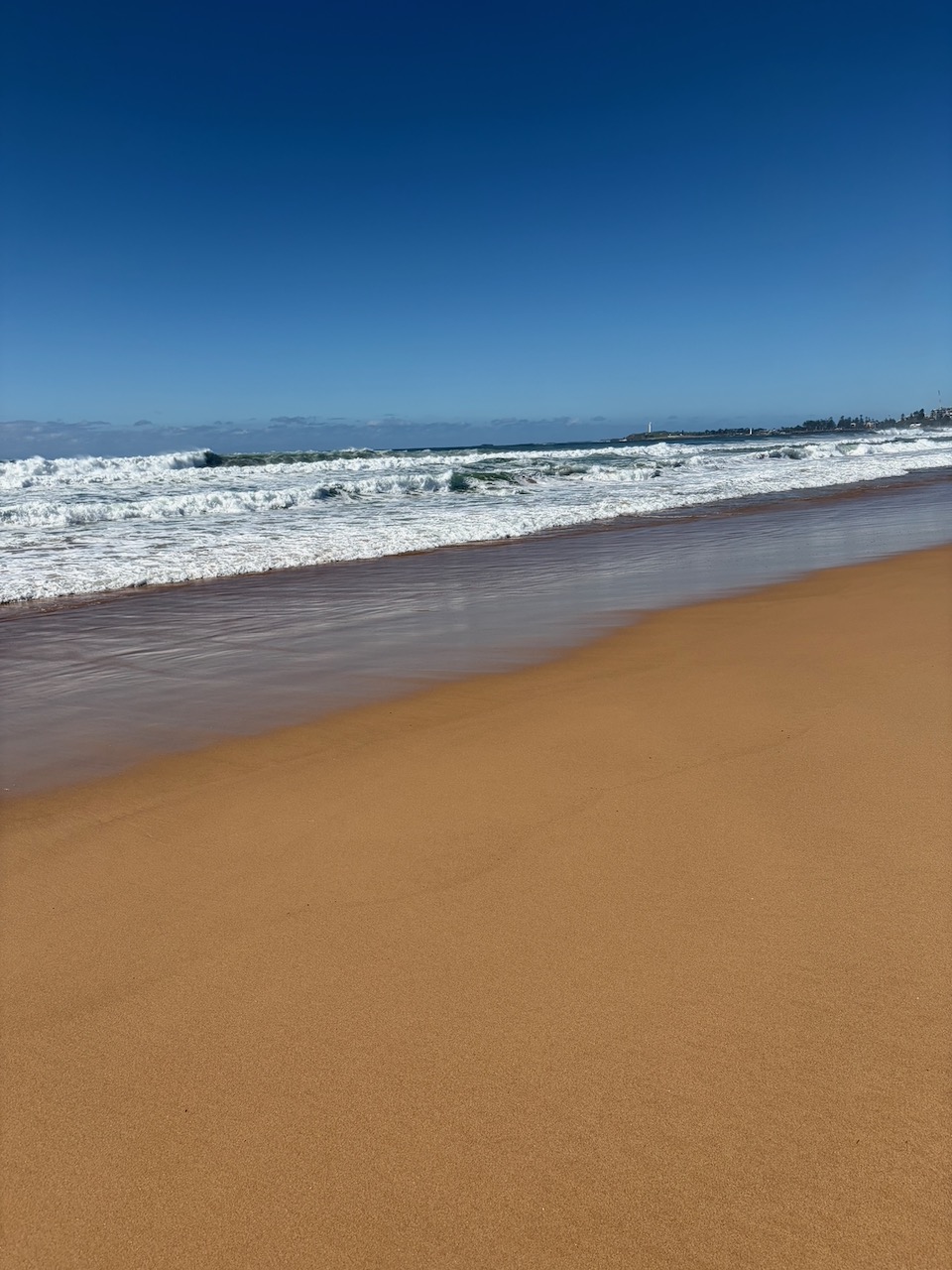 Waves breaking along the beach near Wollongong and Port Kembla under a clear blue sky.