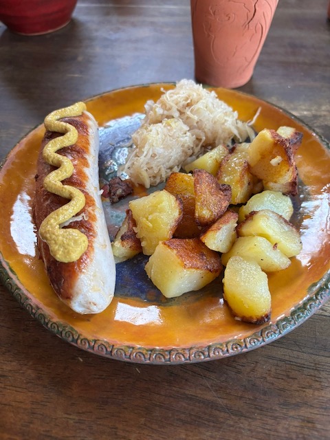 A pottery plate with bratwurst, sauerkraut and Bratkartoffeln served at Pilliga Pottery.