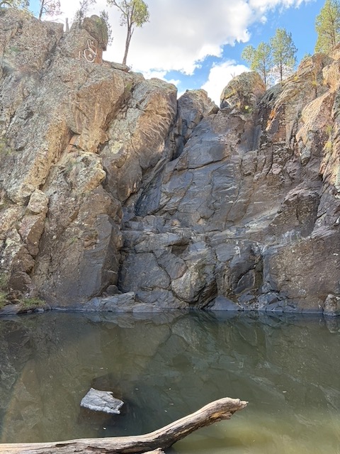 A still dark waterhole at Hickeys Falls surrounded by boulders and rock walls, with trees above.