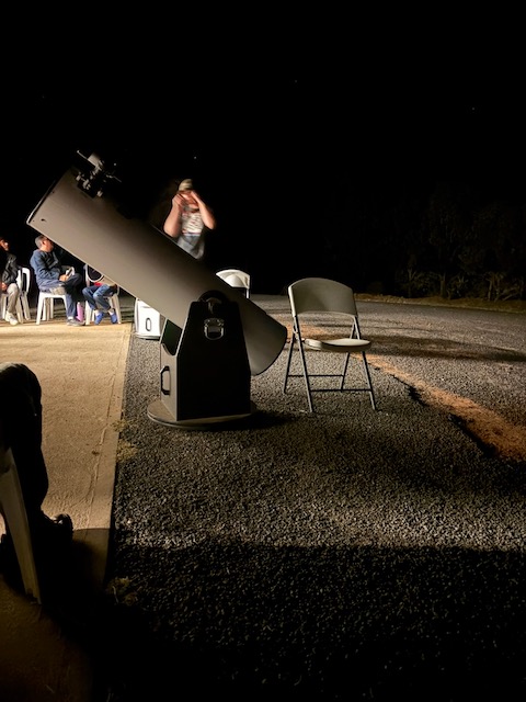 A large Dobsonian telescope set up in the dark at the Warrumbungle stargazing session, with people seated nearby.