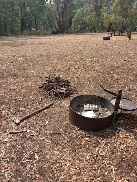 A fire ring with a large axe and pile of kindling beside it at Camp Blackman, in dry eucalyptus woodland.