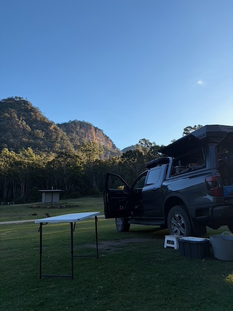 Roger the Ranger parked at Coorongooba campsite under a clear blue sky, sandstone cliffs catching the morning sun behind.